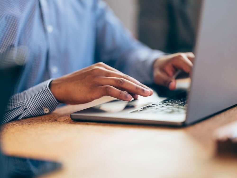 Mãos digitando em um notebook sobre uma mesa de madeira