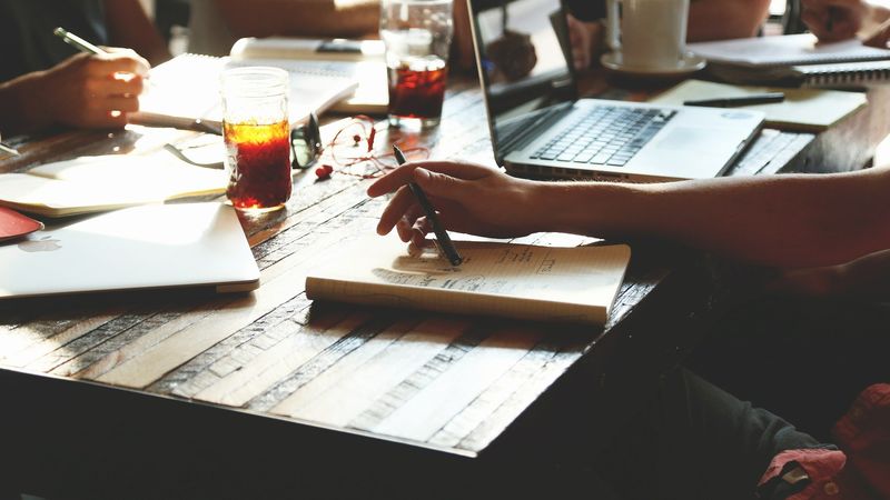 Pessoas trabalhando ao redor de uma mesa com cadernos e notebooks